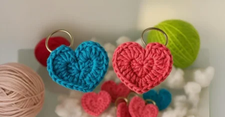 Chaveiro de coração em crochê feito com pontos simples, ideal para lembrancinhas e presentes artesanais, acompanhado de novelos ao fundo.